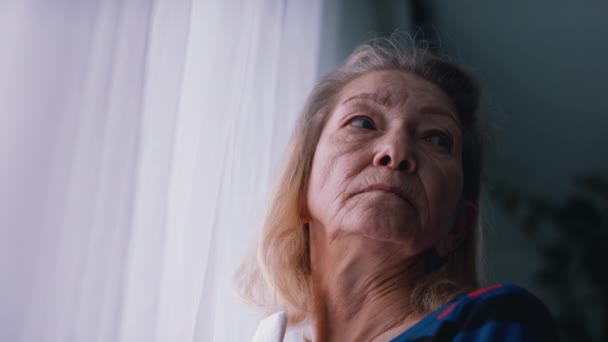 Portret van eenzame oudere vrouw die door het raam kijkt - Video
