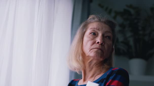 Stara, zamyślona kobieta myśląca przy wielkim oknie. Zdrowie psychiczne i samotność podczas ogniska choroby wietrznej - Materiał filmowy, wideo