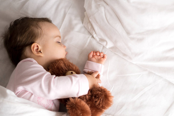 Authentic portrait cute caucasian little infant chubby baby girl or boy in pink sleep with teddy bear on white bed. child resting at lunchtime. care, Sleeping kid, Childhood, Parenthood, life concept - Foto, imagen