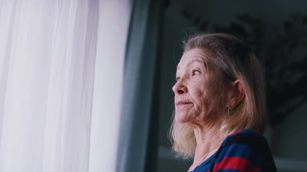 大きな窓の近くで考えている無慈悲な老婦人。感染症発生時の精神的健康とオンライン - 映像、動画
