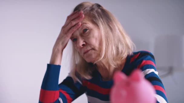 Worried old woman thinking in front of empty piggy bank. Low pension - Footage, Video