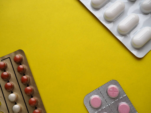Heap of pills on yellow background. Tablets, vitamins and blisters with capsules for the treatment of diseases. Copy space - Photo, image