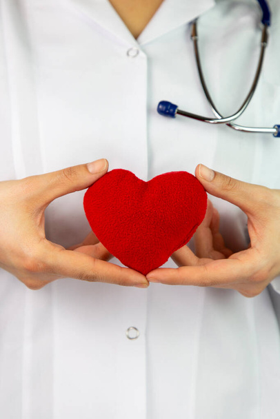 Ženský doktoři drží rudý srdce a dávají k němu stetoskop. Lékařská pomoc nebo pojetí pojištění. Kardiologická péče a zdraví. Heart surgery and resuscitation concept - Fotografie, Obrázek