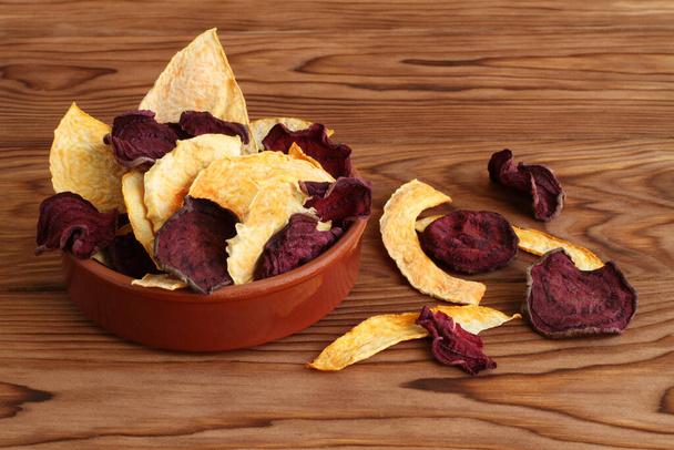 Mix of dried beetroot and pumpkin vegetable crisps lying in ceramic bowl on a wooden table. Closeup. Macro - Photo, image