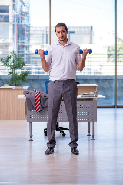 Jovem funcionário do sexo masculino fazendo exercícios esportivos no escritório - Foto, Imagem