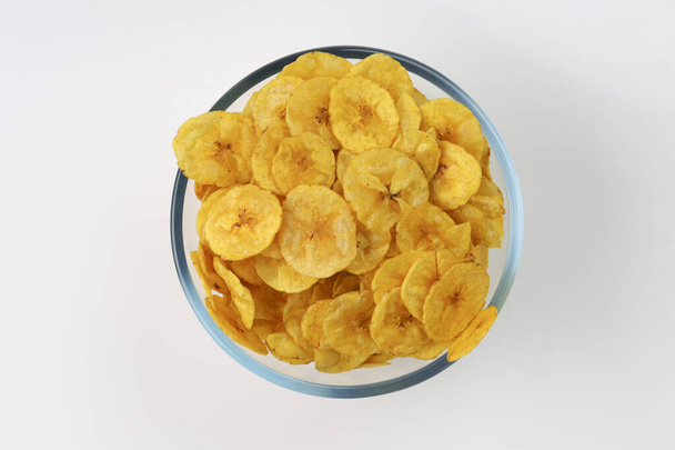 Suszone chipsy bananowe lub gofry bananowe, pięknie ułożone w szklanej misce z białym, teksturowanym tłem, izolowane. - Zdjęcie, obraz