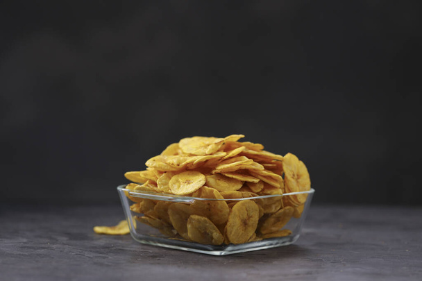 Dried banana chips or banana waffers,arranged beautifully in a glass bowl or tableware  with grey  textured background, isolated. - Photo, Image