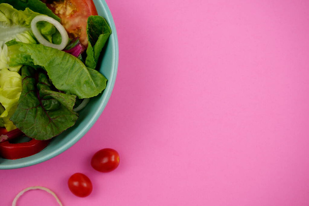健康的で栄養価の高い食事。野菜サラダ。菜食主義者だ。空間とピンクの背景に緑のボウルに食品。トップビュー、水平、オフセンタースタイル。まだ生活、食べ物の写真. - 写真・画像