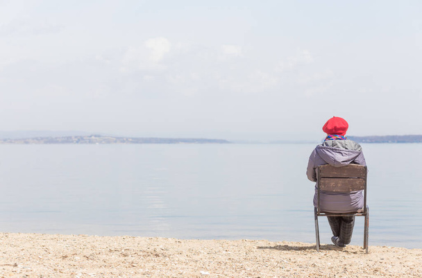 Elderly woman admires sea view on a beach in sunny day. Travel concept. Loneliness concept. - Fotoğraf, Görsel