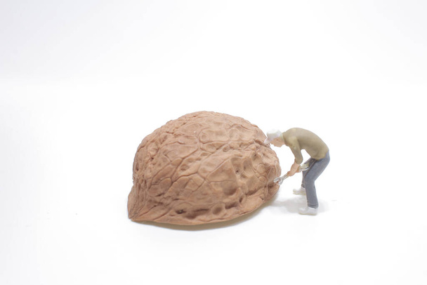 Miniaturní pracovník s páčidlem se snaží otevřít ořech - Fotografie, Obrázek
