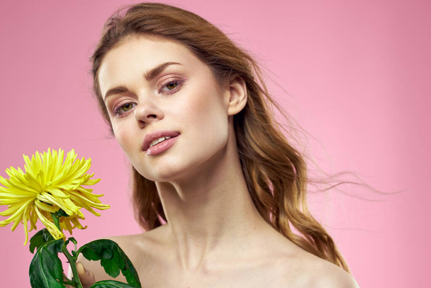Kaunis nainen alasti hartiat keltainen kukka charmia kosmetiikka vaaleanpunainen tausta - Valokuva, kuva