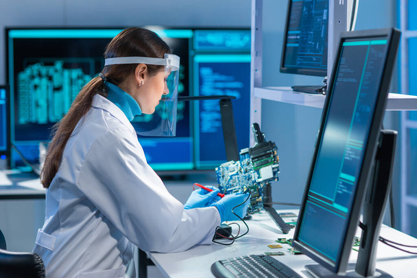 Female microelectronics engineer works in a scientific laboratory on computing systems and microprocessors. Professional electronic factory worker is testing the motherboard and coding the firmware. - Foto, Imagem