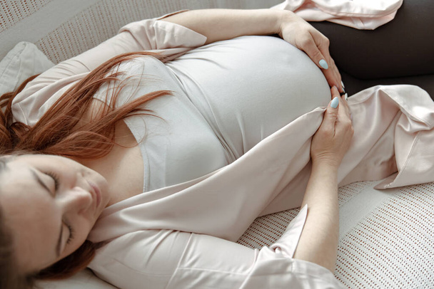 Κομψή έγκυος γυναίκα τον τελευταίο μήνα ξεκουράζεται στον καναπέ στο σπίτι κοντά. - Φωτογραφία, εικόνα