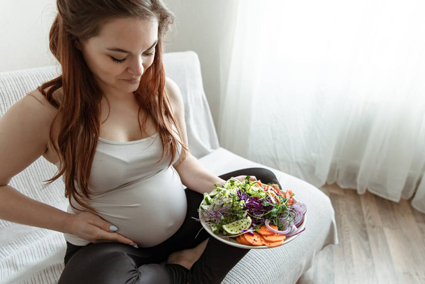 La futura mamma negli ultimi mesi di gravidanza sta tenendo un piatto di insalata di verdure.. - Foto, immagini