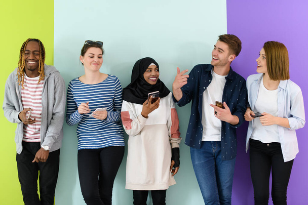 a group of diverse teenagers use mobile devices while posing for a studio photo in front of a pink background. - Foto, imagen