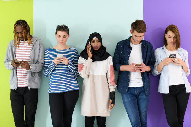 a group of diverse teenagers use mobile devices while posing for a studio photo in front of a pink background. - Fotoğraf, Görsel
