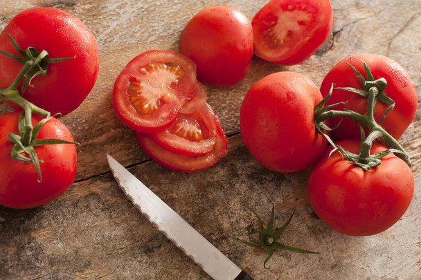 High-angle close-up view of fresh and juicy tomatoes as a nutritious ingredient next to a knife on a rustic wooden table - Photo, Image