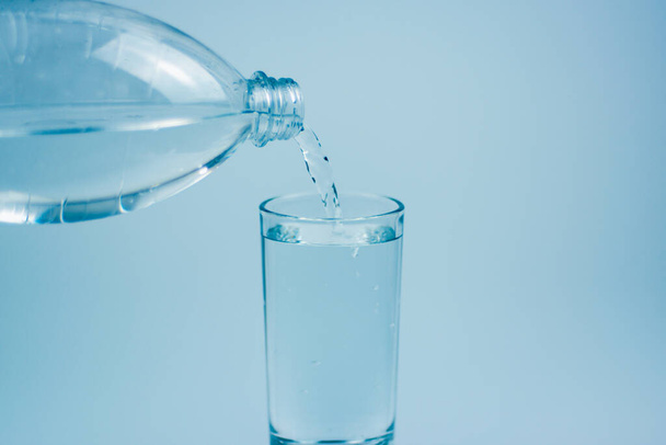 Pouring drink water into glass on light blue background. - Foto, Imagen