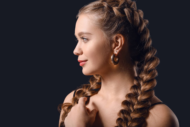 Schöne junge Frau mit geflochtenen Haaren auf dunklem Hintergrund - Foto, Bild