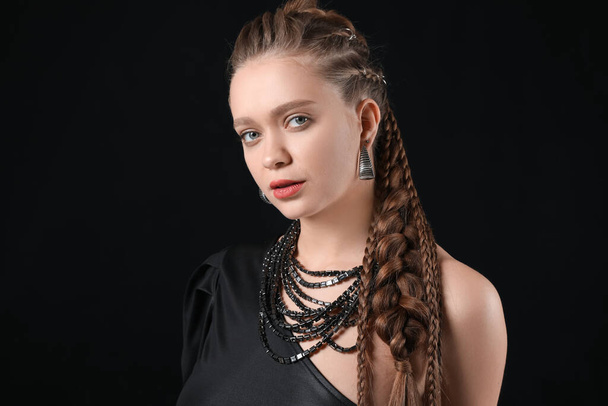 Schöne junge Frau mit geflochtenen Haaren auf dunklem Hintergrund - Foto, Bild