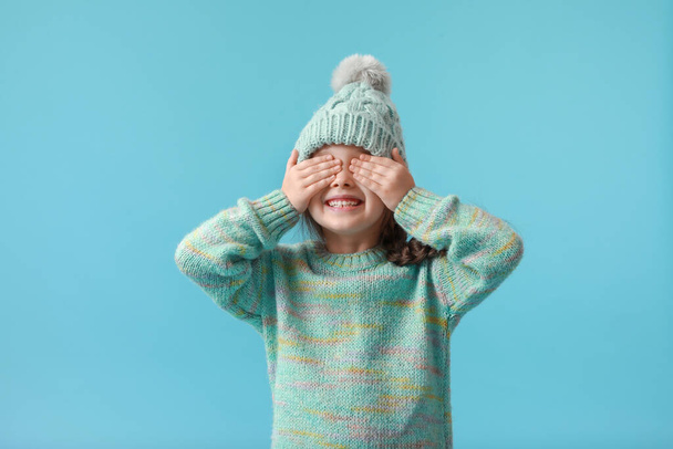 Little girl in winter clothes covering eyes with her hands on color background - Photo, image