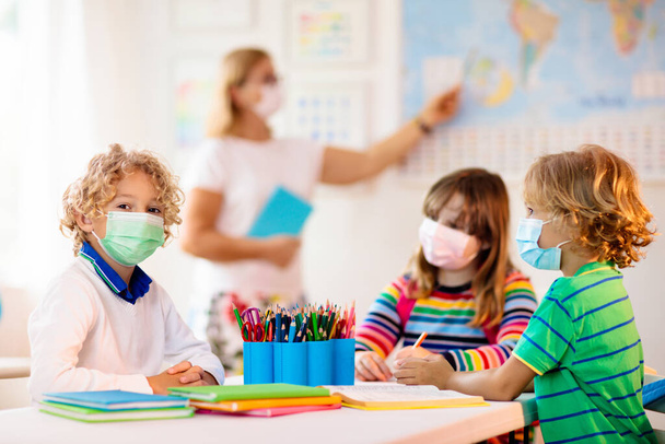 Teacher in class, school child in face mask during corona virus and flu outbreak. Boy and girl back to school after covid-19 quarantine and lockdown. Group of kids in masks for coronavirus prevention. - Photo, Image