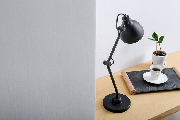 Modern lamp and cup of coffee on table near light wall in room - Photo, Image