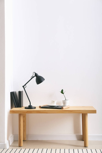 Moderne Lampe und Tasse Kaffee auf dem Tisch in der Nähe der Lichtwand im Zimmer - Foto, Bild