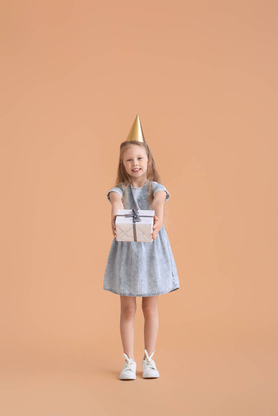 Nettes kleines Mädchen in Partyhut und mit Geschenk auf farbigem Hintergrund - Foto, Bild