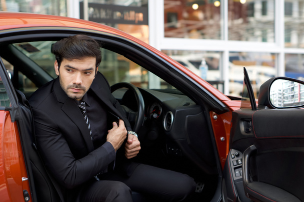 Young caucasian businessman in  black suit step down from a bright sports car while put his mobile phone into suit pocket. - Φωτογραφία, εικόνα
