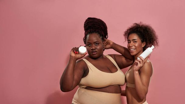 A plus size girl poses together with her female friend in front of the pink wall - Fotoğraf, Görsel