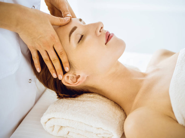 Beautiful woman enjoying facial massage with closed eyes in spa center - Photo, image