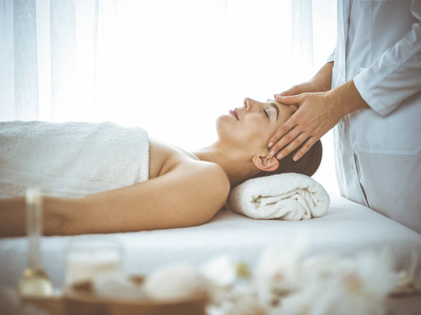 Beautiful brunette woman enjoying facial massage with closed eyes comfortable and blissful. Relaxing treatment in medicine and spa center concepts - Φωτογραφία, εικόνα
