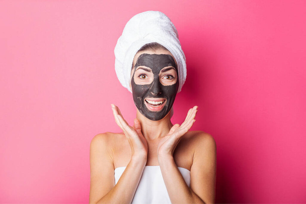 surprised smiling young woman with black mask on her face on a pink background. - Foto, afbeelding