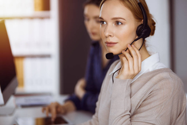 Businesswoman talking by headset in office. Call center and diverse people group in business - Fotoğraf, Görsel