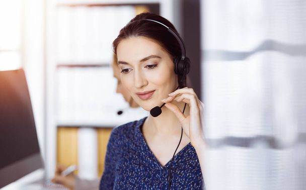 Latin american businesswoman talking by headset in office. Call center and diverse people group in business - Photo, Image