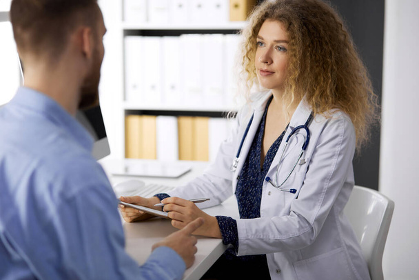 Female doctor and man-patient discussing current health examination while sitting in clinic. Perfect medical service and medicine concept - Photo, Image