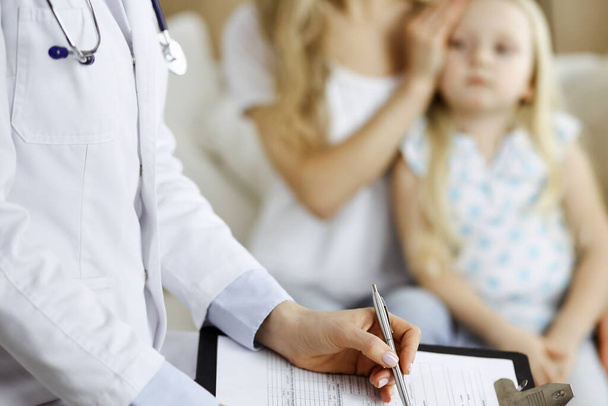Doctor and patient. Pediatrician using clipboard while examining little girl with her mother at home. Sick and unhappy child at medical exam. Medicine concept - 写真・画像