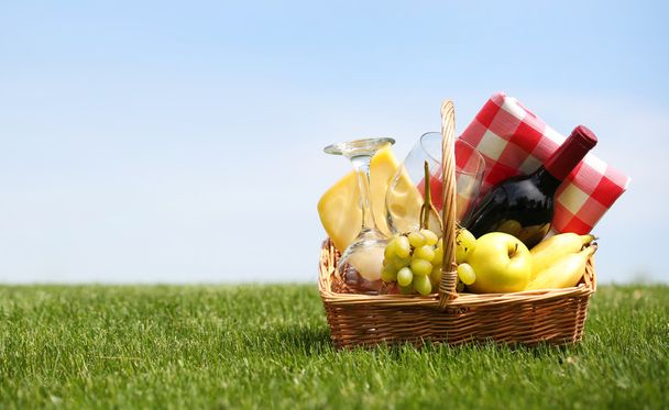 Picnic basket with food on green grass over blue sky - Photo, image