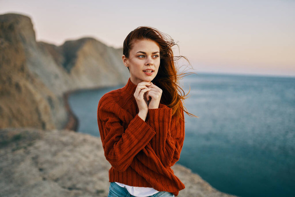 γυναίκα σε ένα κόκκινο πουλόβερ στα βουνά κοντά στο μοντέλο του θαλάσσιου τουρισμού - Φωτογραφία, εικόνα