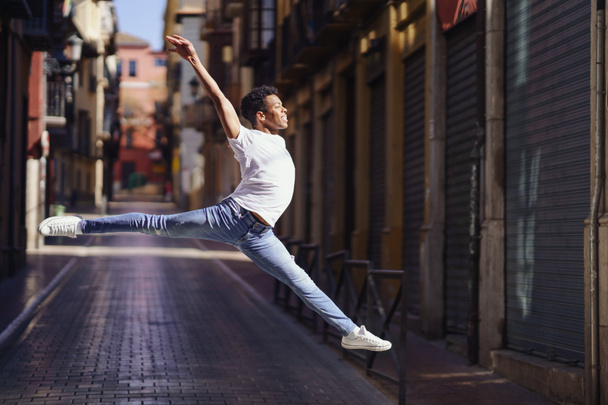 Chico negro feliz haciendo un salto acrobático en medio de la calle. - Foto, imagen