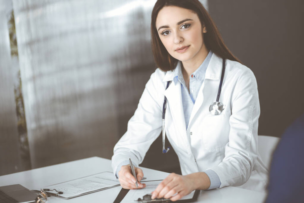 Улыбающаяся молодая женщина-врач заполняет медицинские рекомендации с помощью планшета. Терапевт на работе в клинике. Концепция медицины - Фото, изображение