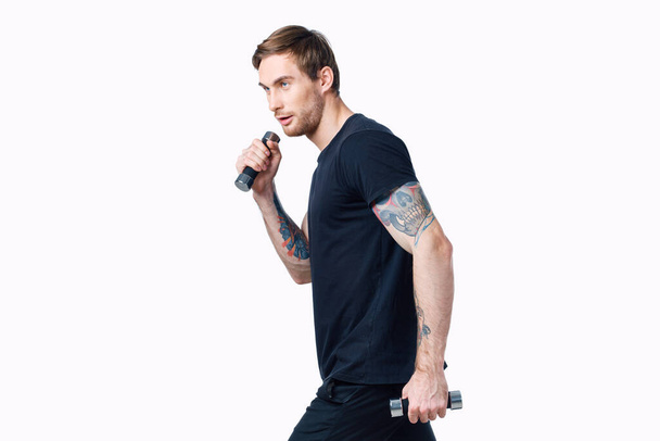 urheilullinen mies käsipainoilla valkoisella taustalla hänen tatuointi käsivarteen musta t-paita rajattu näkymä - Valokuva, kuva