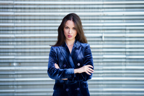 Kobieta w niebieskim garniturze pozuje w pobliżu nowoczesnego metalowego budynku. - Zdjęcie, obraz