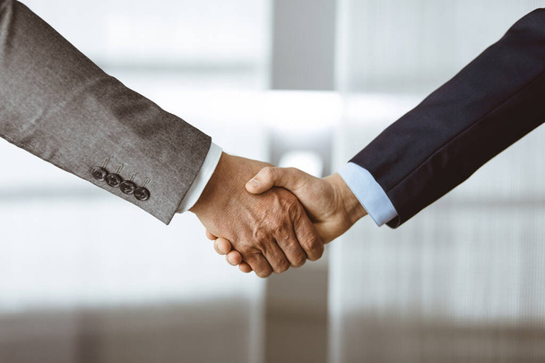Business people in office suits standing and shaking hands, close-up. Business communication concept. Handshake and marketing - 写真・画像