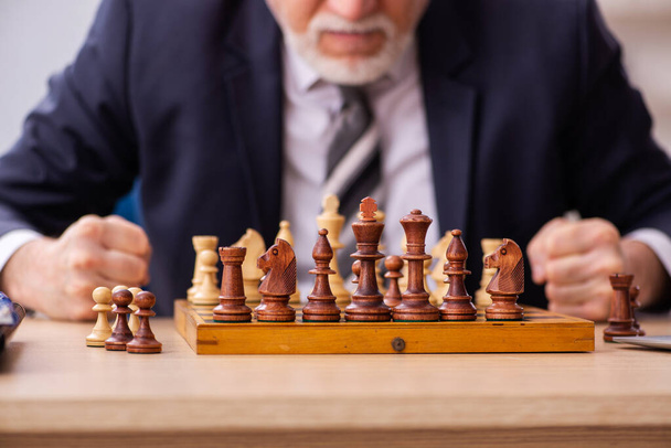 Old male employee playing chess at workplace - Zdjęcie, obraz