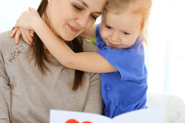 Mothers day concept. Child daughter congratulates mom and gives her postcard with red heart shape. Mum and girl happy smiling and hugging. Family fun and holiday - Zdjęcie, obraz
