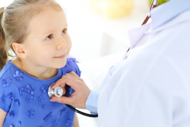 Doctor examining a little girl by stethoscope. Happy smiling child patient at usual medical inspection. Medicine and healthcare concepts - Foto, imagen