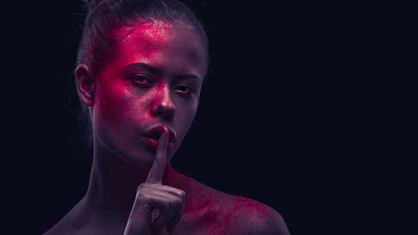 Woman in artistic makeup on dark background, Showing shhhhhh emotion, holding finger at mouth - Foto, Imagem
