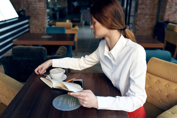nainen hame paita pöydässä kahvilassa kahvi kuppi kädessä ja muistilehtiö kynä - Valokuva, kuva